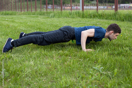 Outdoor fitness workout. Young man doing an exercise in the city park, performing push ups on the grass