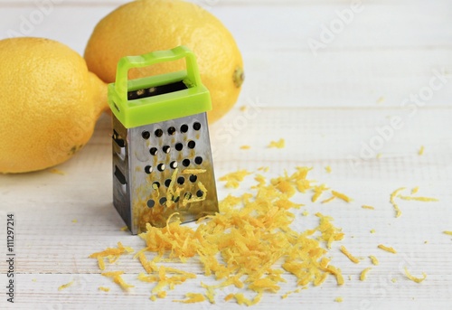Peeling lemon zest. Small grater, citrus fruit, yellow, zest cuttings, white table. Close-up, soft focus. 