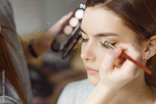 Young woman applying makeup to model in salon