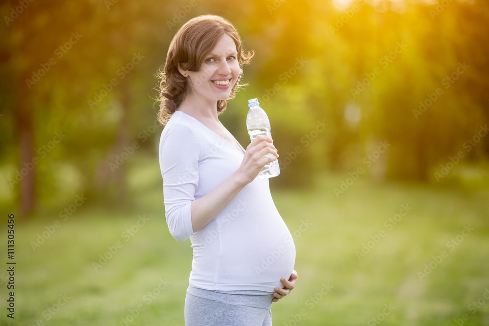 Portrait of happy pregnant woman posing with bottle of water in Portrait of happy pregnant woman posing with bottle of water in