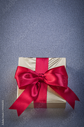Present box wrapped in glittery paper with red bow on grey backg