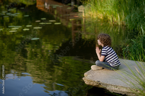 Fototapeta Naklejka Na Ścianę i Meble -  Little boy sits cross-legged on the lake.