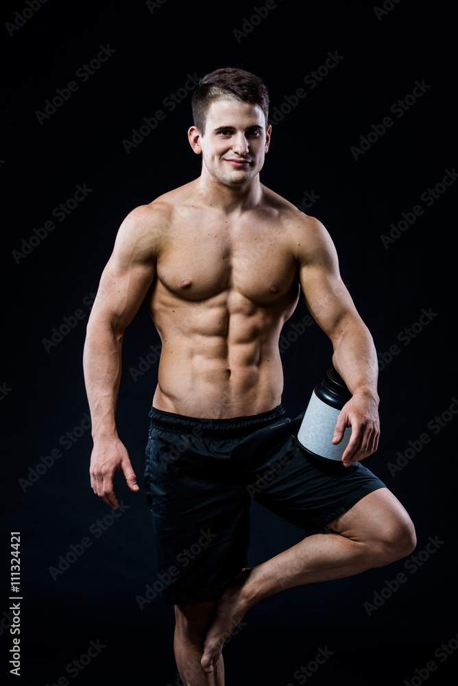 Bodybuilding and Sports theme: handsome strong bodybuilder holding plastic jar with a dry protein feeling relaxed isolated on black background in studio