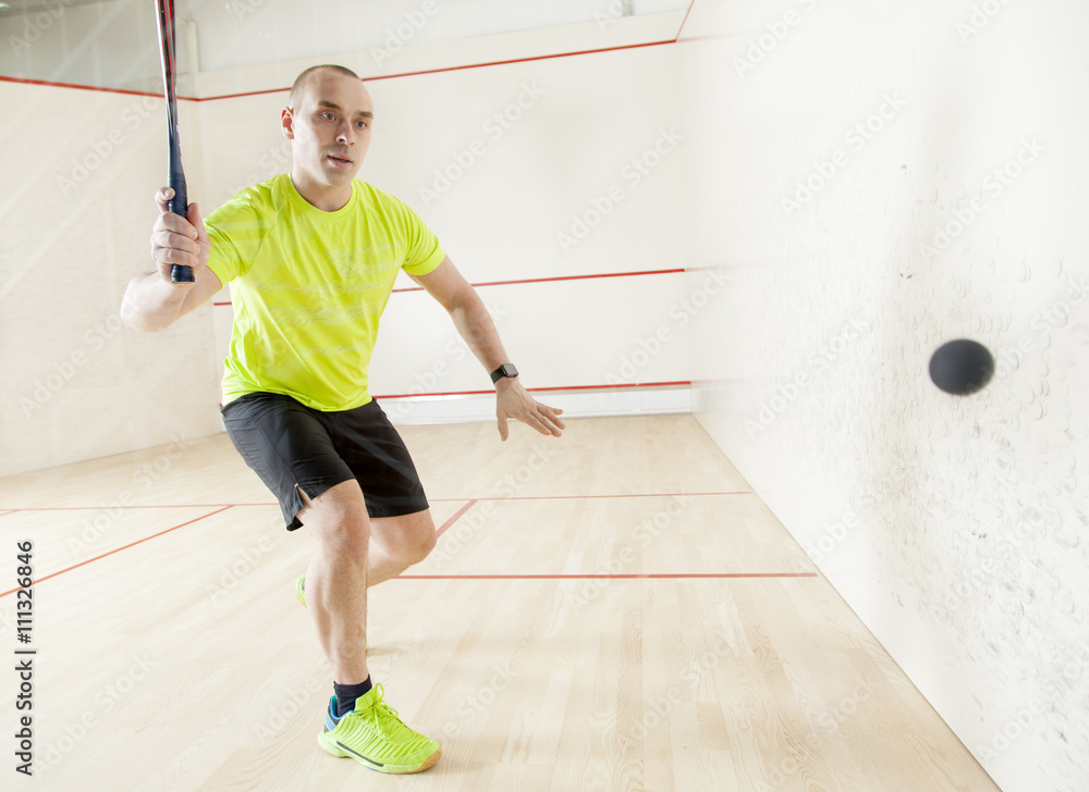 Young Caucasian man in a yellow T-shirt playing squash.