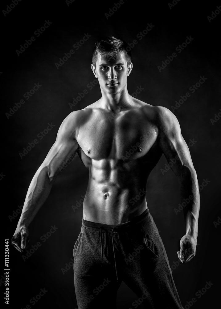 Fototapeta premium Sexy shirtless bodybuilder posing, looking at camera on black ba