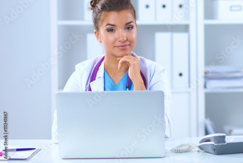 Female doctor sitting on the desk and working a laptop in hospital