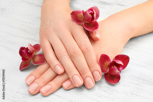 Woman hands with beautiful manicure and purple orchid on wooden background, close up