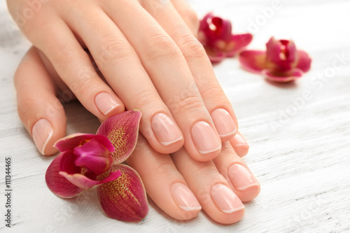Woman hands with beautiful manicure and purple orchid on wooden background  close up