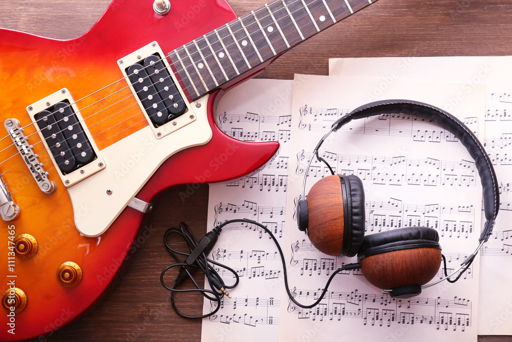 Naklejka premium Electric guitar with notes and headphones on wooden background