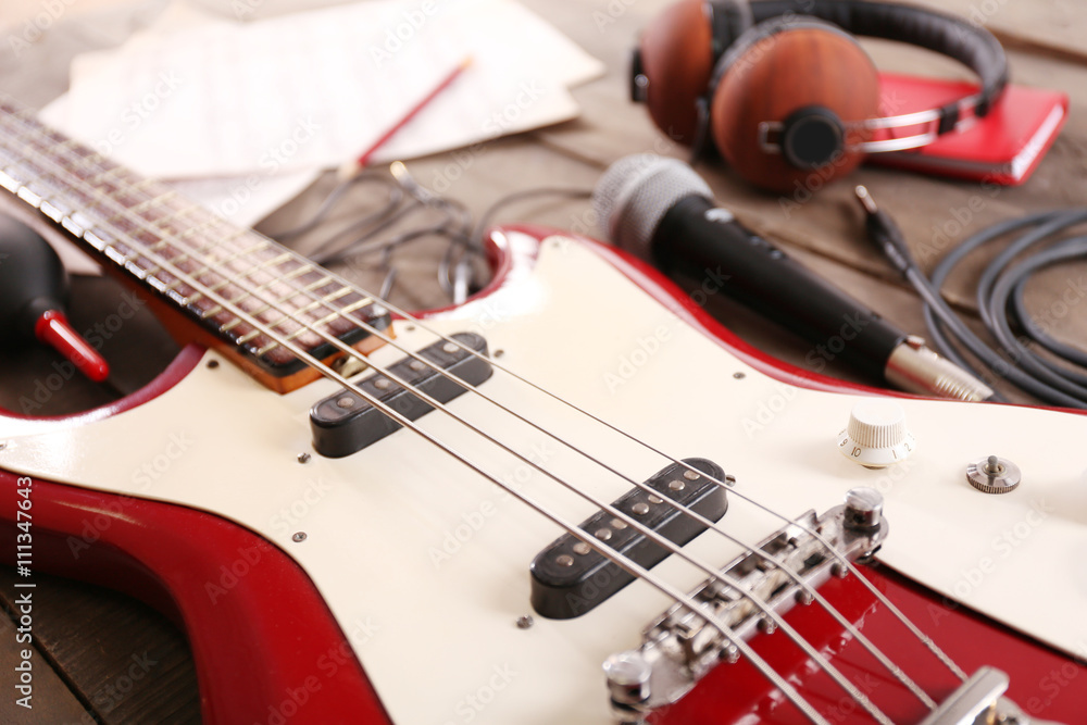 Fototapeta premium Electric guitar with notes, microphone and headphones on wooden background