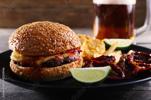 Big tasty hamburger with snacks and glass mug of light beer on wooden table