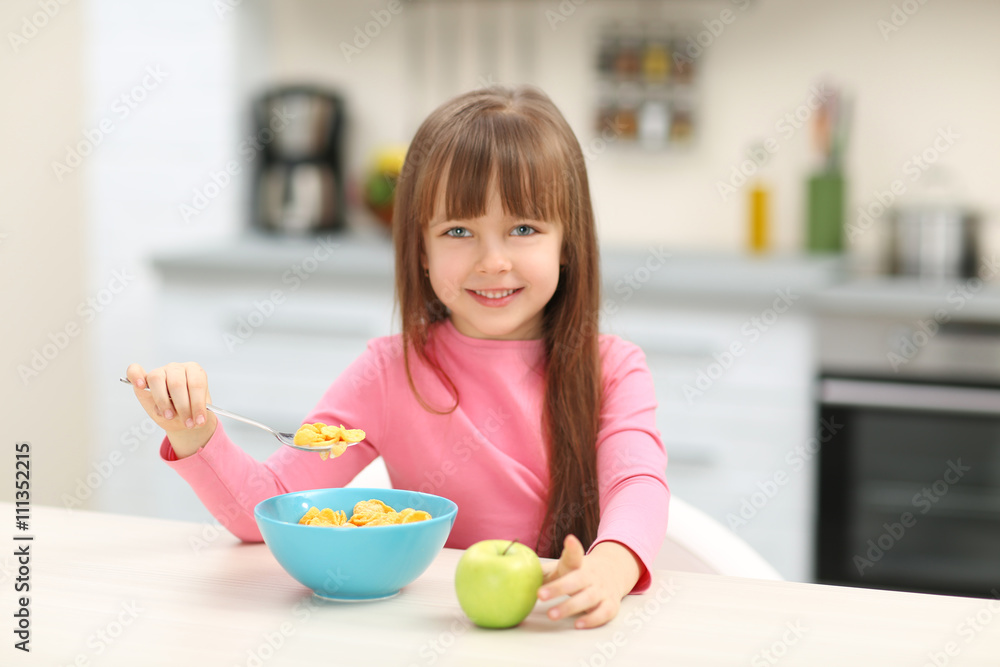 Beautiful little girl having breakfast with cereal and apple in kitchen Beautiful little girl having breakfast with cereal and apple in kitchen