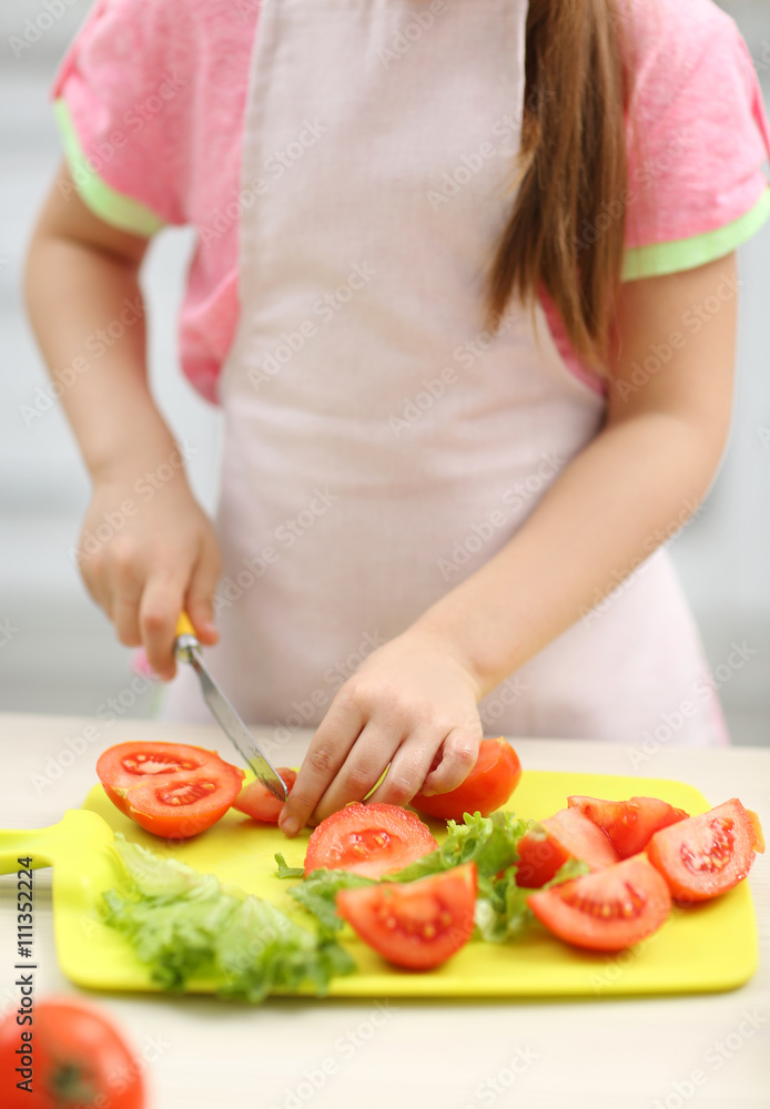 Little girl cutting vegetables for the salad in the kitchen Little girl cutting vegetables for the salad in the kitchen