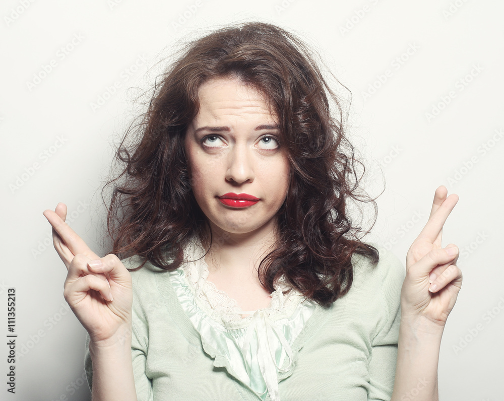 smiley woman hoping hard with fingers crossed against gray backg smiley woman hoping hard with fingers crossed against gray backg