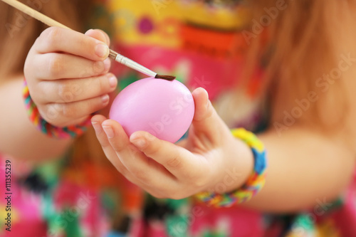 Little girl decorating Easter egg closeup