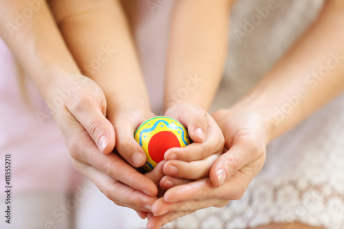 Hands of mother and daughter holding decorated Easter egg closeup