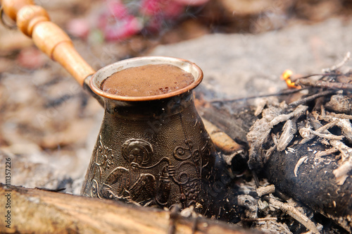 Hot coffee prepared in turk on open fire. Closeup.