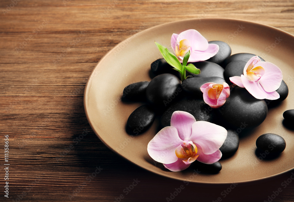 Spa stones and orchid flowers in plate on wooden background Spa stones and orchid flowers in plate on wooden background
