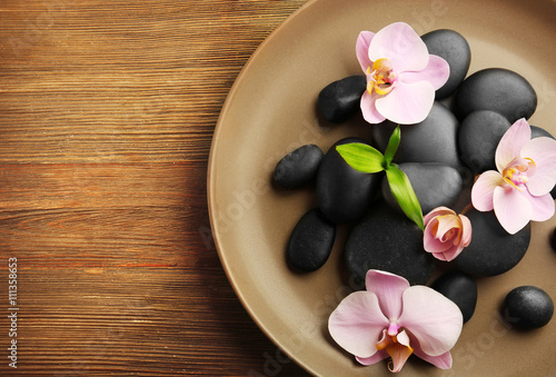 Spa stones and orchid flowers in round plate, top view