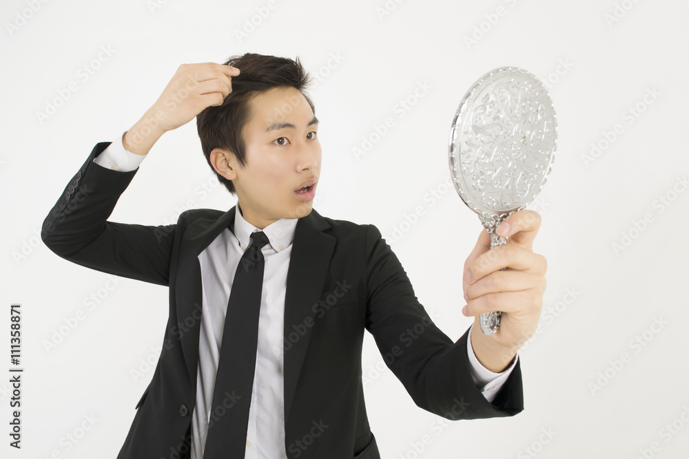 Asian young businessman in a black suit, looking at himself in a hand mirror Asian young businessman in a black suit, looking at himself in a hand mirror