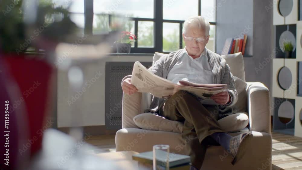 elderly man sits in a chair and reading a newspaper in a modern apartment