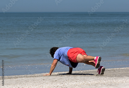 Senior woman stretching and exercising on a sunny morning on a Gulf Coast beach.
