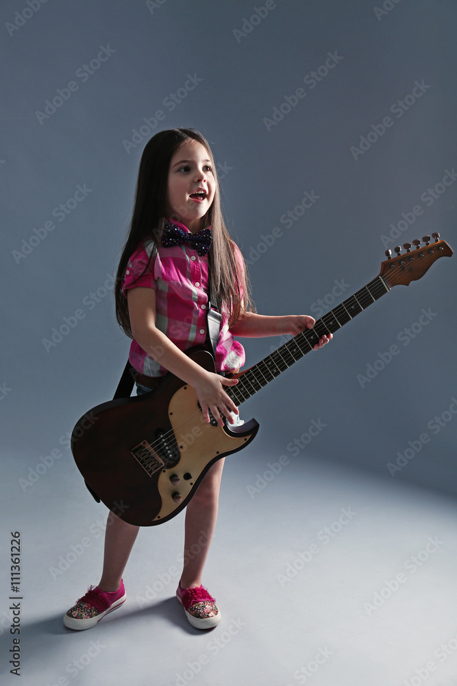 Beautiful artistic little girl playing guitar on grey background Beautiful artistic little girl playing guitar on grey background