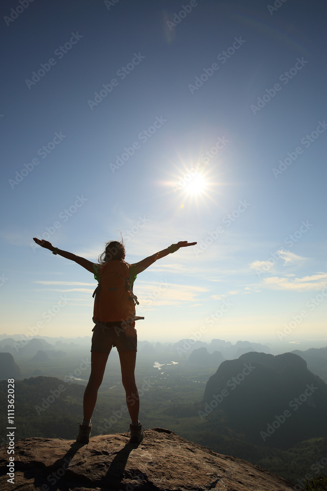 cheering woman hiker open arms at sunrise mountain peak