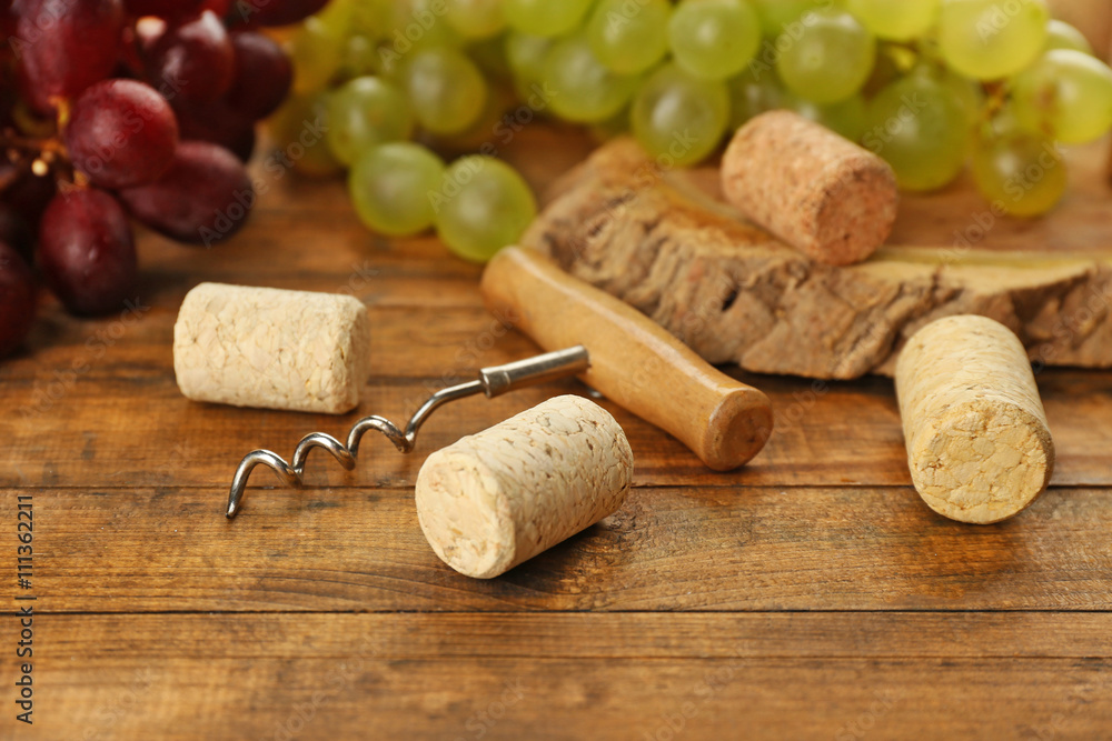 Wine corks and tailspin with grapes on wooden background