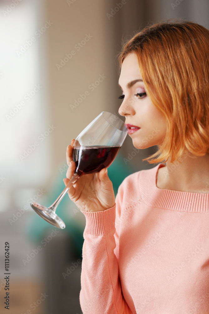 Young woman with glass of red wine on light blurred background