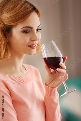 Young woman with glass of red wine on light blurred background