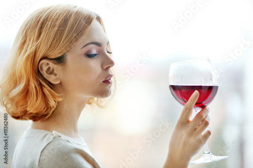 Young woman with glass of red wine on light blurred background