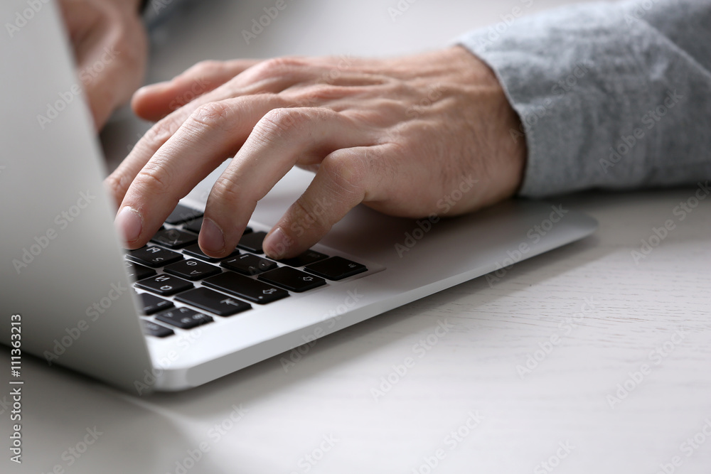 Male hands typing on laptop keyboard at table closeup Male hands typing on laptop keyboard at table closeup