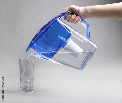 A hand pouring filtered water in the glass, on the grey background