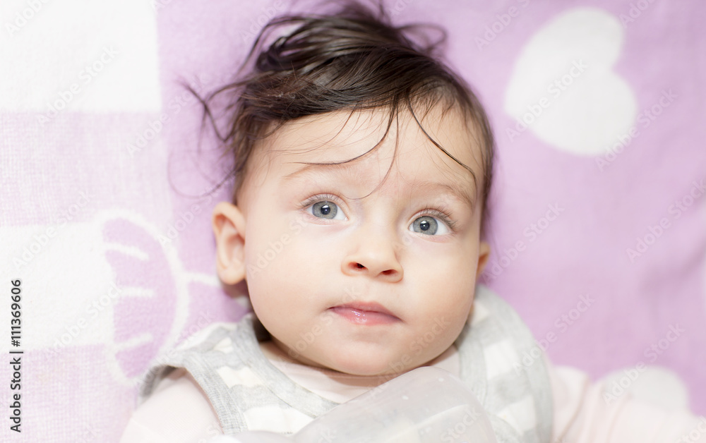 Portrait of little girl close up while the meal. Six-month old baby lying on his back and drinking from the baby bottle. A child plays with a baby bottle, self-indulgence.