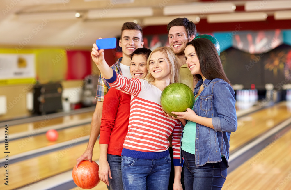 Fototapeta premium happy friends with smartphone in bowling club