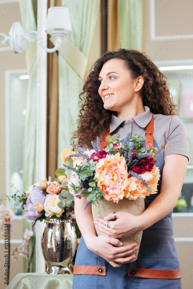 Smiling woman florist holding vase with flowers in the shop