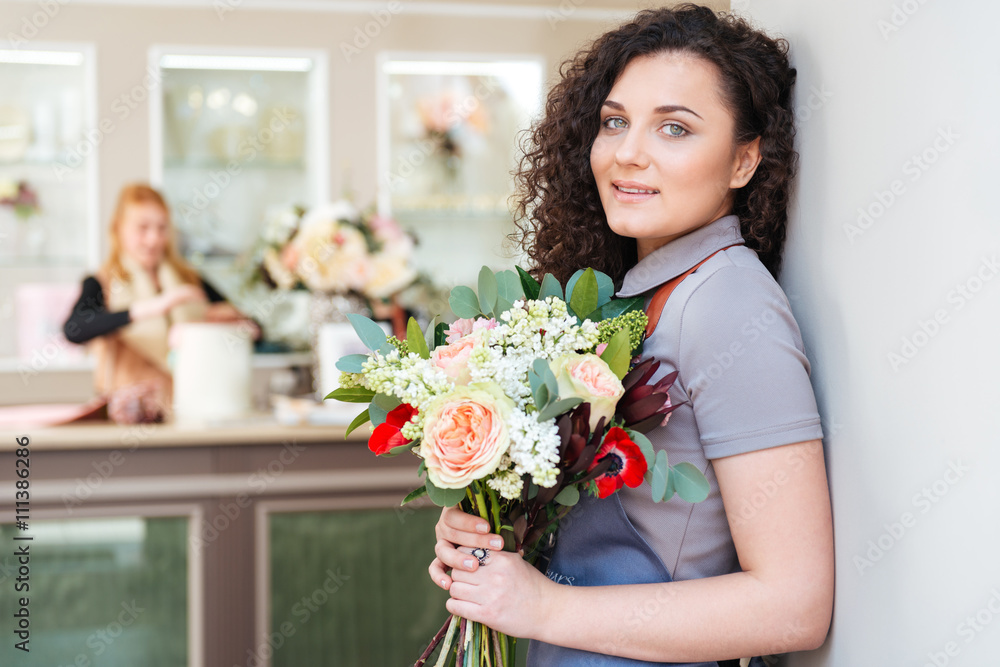 Woman florist with bouquet of flowers standing in flower shop