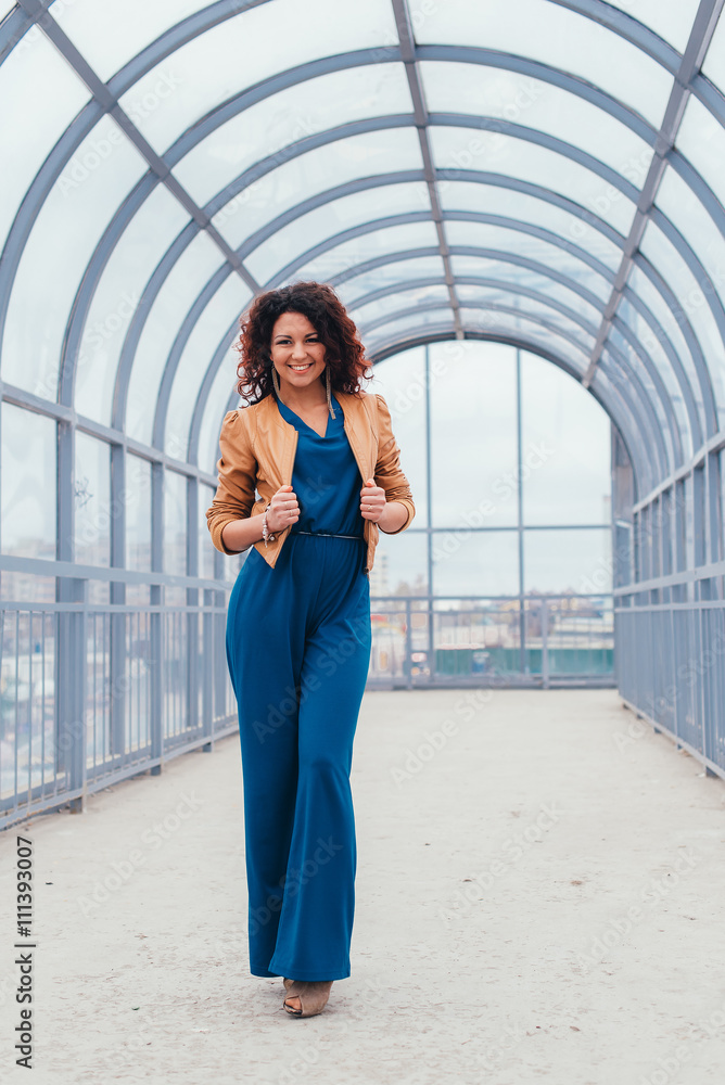 Beautiful curly-haired woman in a long dress on a light background