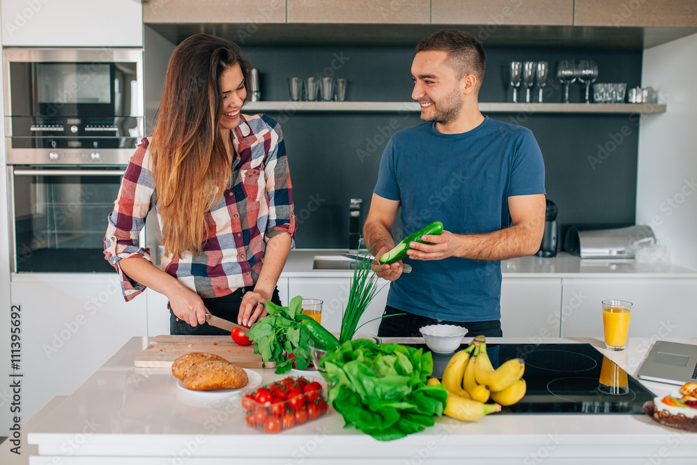 Young couple preparing salad in the kitchen. They are cutting to Young couple preparing salad in the kitchen. They are cutting to