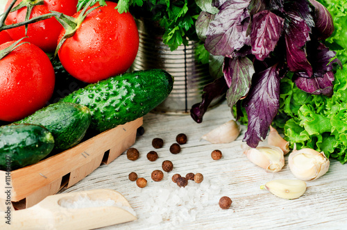  Fresh juicy ripe summer useful vegetables and greens, red tomatoes , cucumbers , cabbage , lettuce , basil , parsley , dill and salt and spices on a wooden background