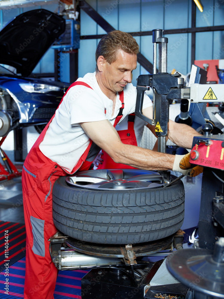 Fototapeta premium Car mechanic with tyre lever is fitting a tyre