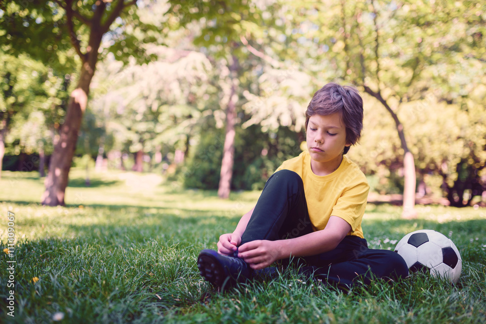 Boy Tying Soccer Shoes on Grass Field Boy Tying Soccer Shoes on Grass Field