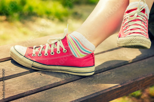 Woman's feet in a bright red canvas sneakers sitting on a bench.