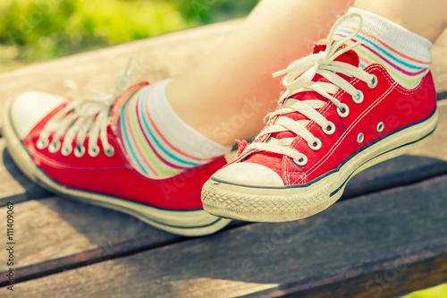 Woman's feet in a bright red canvas sneakers sitting on a bench.