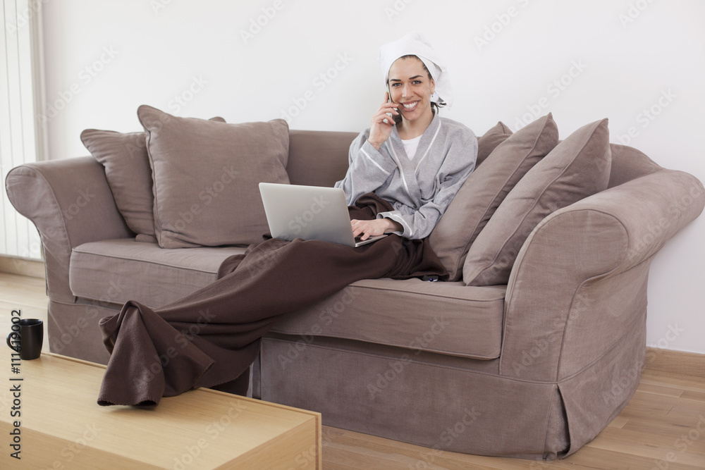 Women wearing bathrobe working on lap top and talking on the phone in living room Women wearing bathrobe working on lap top and talking on the phone in living room