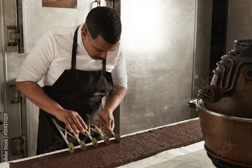 Fotografija Side view black man chief use professional vintage separator to split chocolate