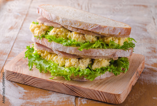 Sandwich with scramble eggs, leaves salad and ham on wooden baskgraund. Selective focus photo