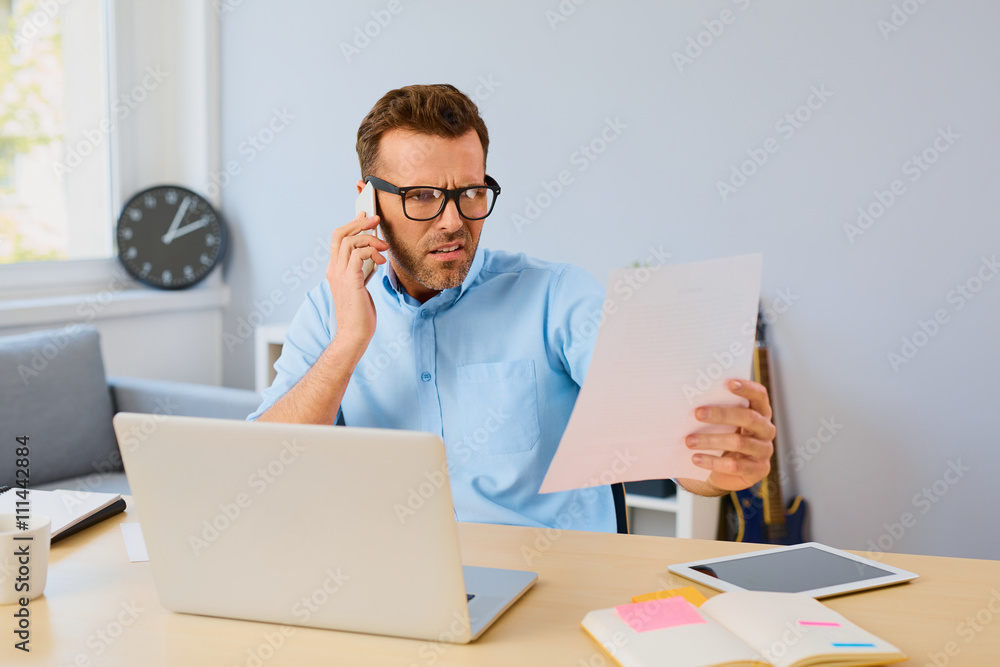 Angry man paying his bills with laptop and talking on phone at Angry man paying his bills with laptop and talking on phone at