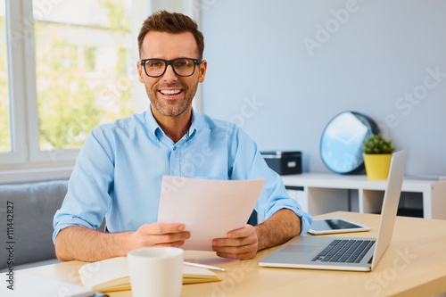 Happy man working from home holding some documents and looking a